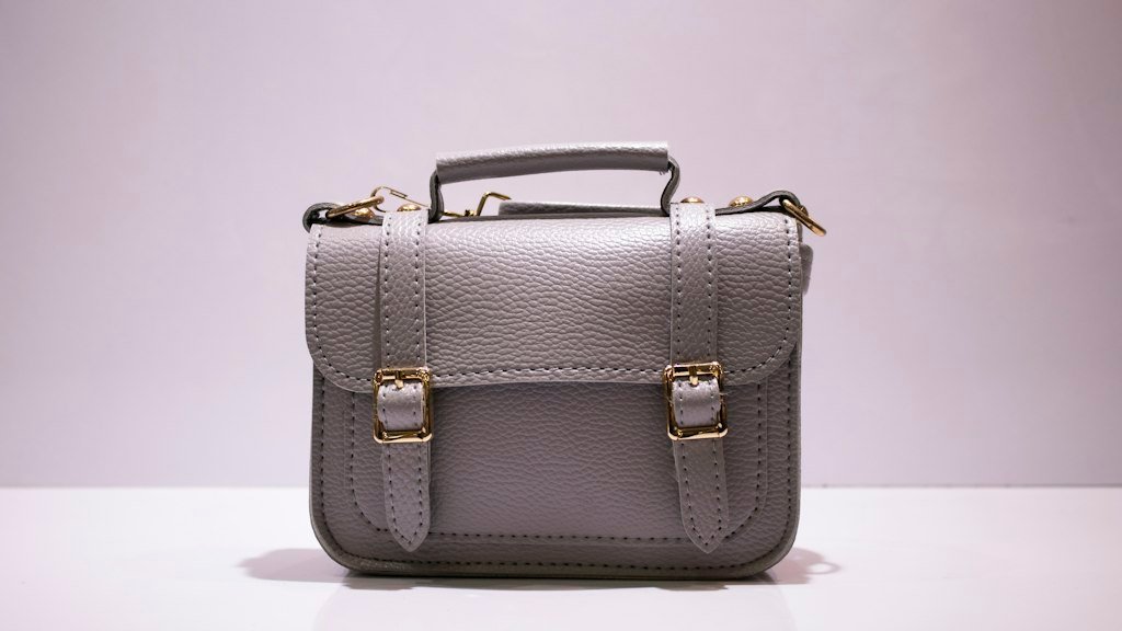 Grey leather satchel with gold buckles on a white surface, a quiet luxury accessory